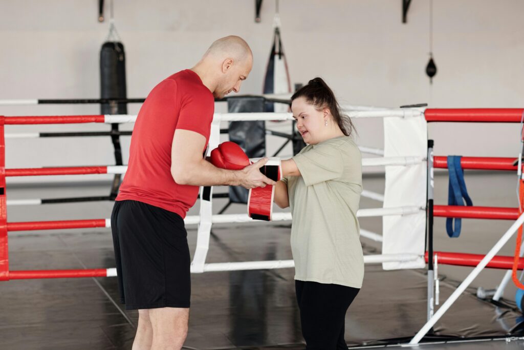 Boxing trainer helping young woman with Down syndrome during a training session in a gym.